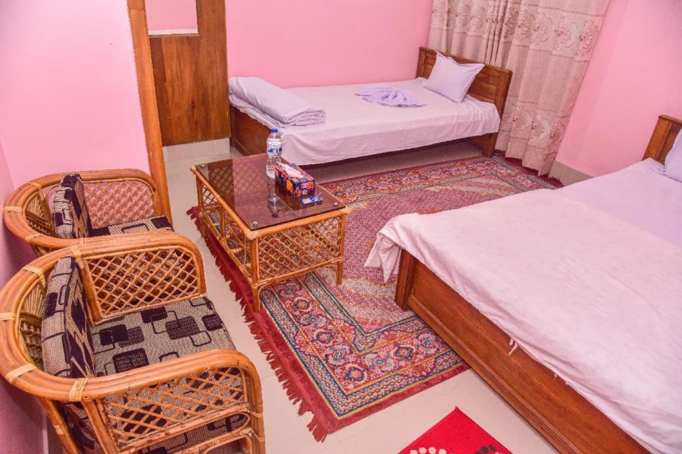 A twin bedroom with pink walls and rattan chairs at Al Hera Resort