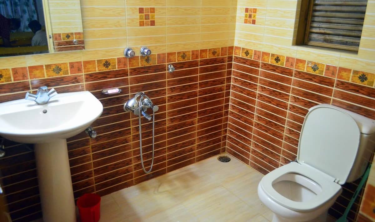 Ensuite bathroom lined in cream and wood-grain tile with a patterned orange border course, a white pedestal basin, wall-mounted hand shower and western toilet