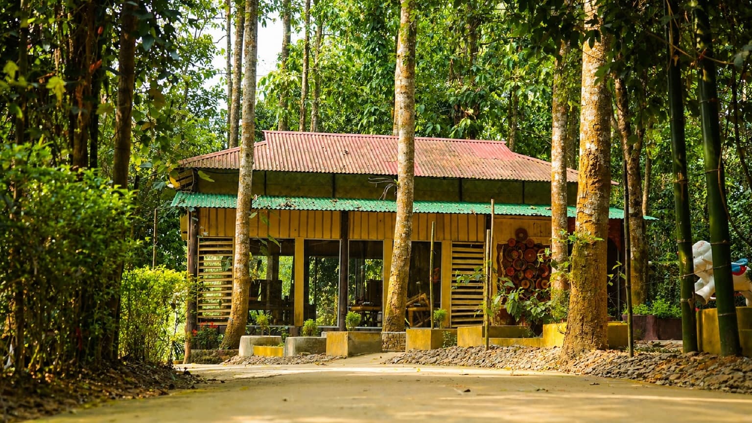 Arannyo Nibas Eco Resort's open-air restaurant building with a red tin roof, set among tall forest trees
