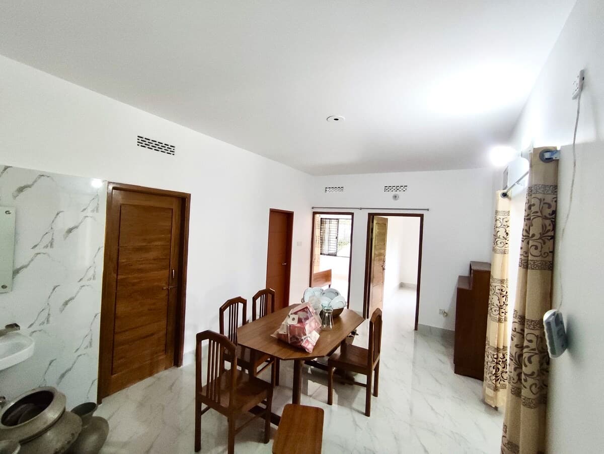 Dining area with a wooden table and six chairs set with dishware, marble-tile flooring, wooden doors, and a hallway leading to a balcony in the background