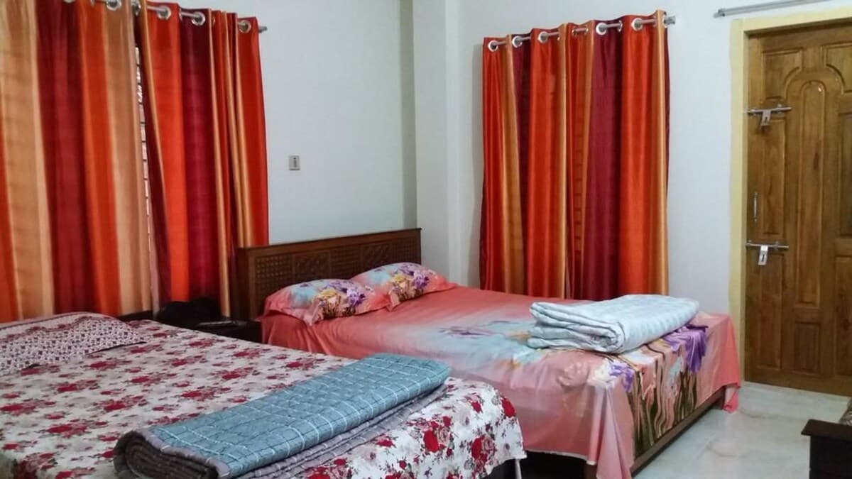 Twin-bed guest room with orange and burgundy curtains, floral pink and white bedding, and a folded grey throw at the foot of each bed