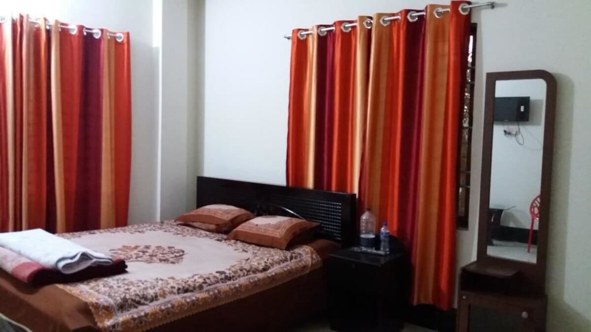 Double bed room with dark wood headboard, orange floral bedspread, wall-mounted TV, and a full-length standing mirror in the corner