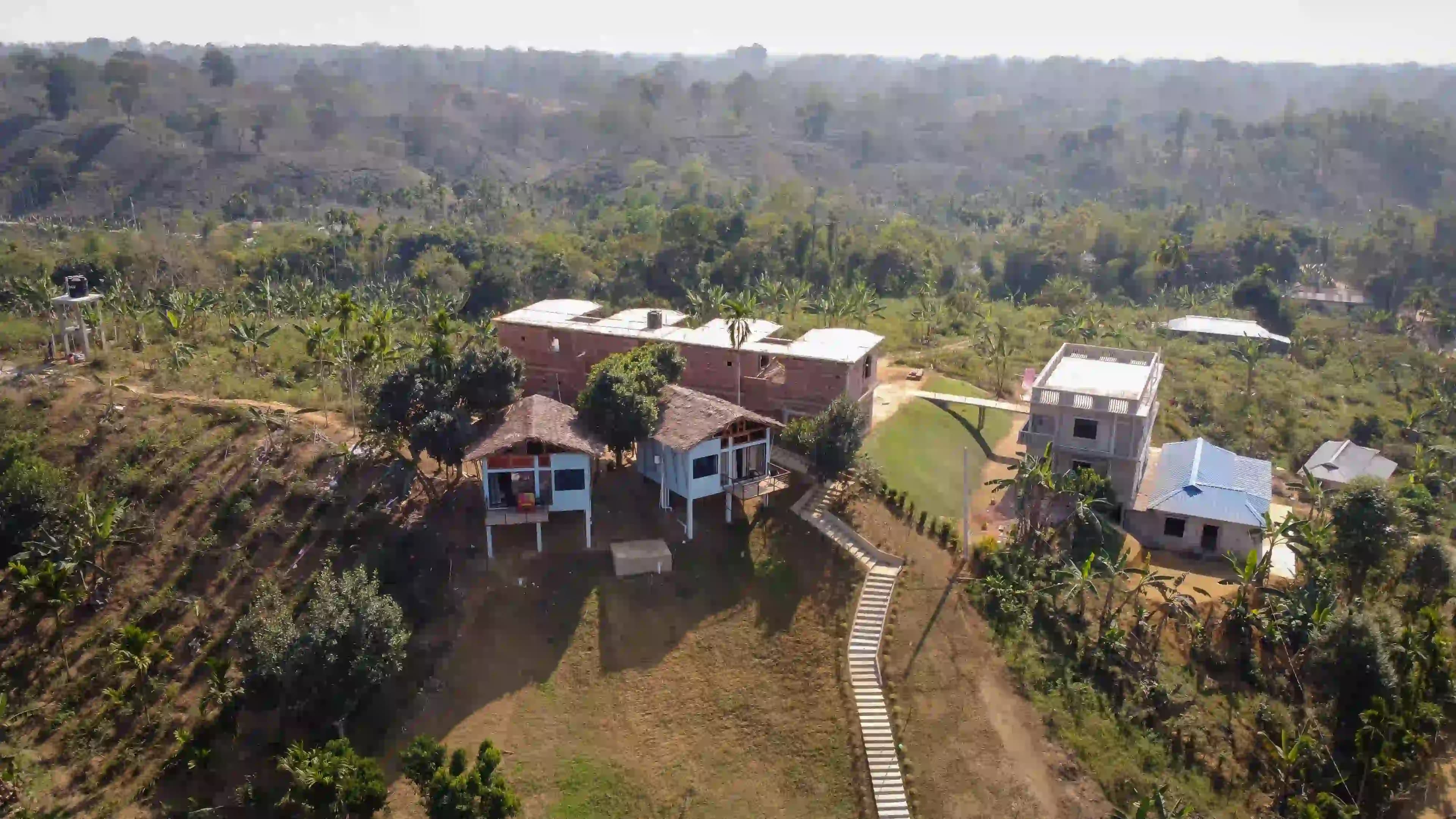 Aerial view of Bonsai Eco Village's stilted cottages and grounds surrounded by hillside farmland