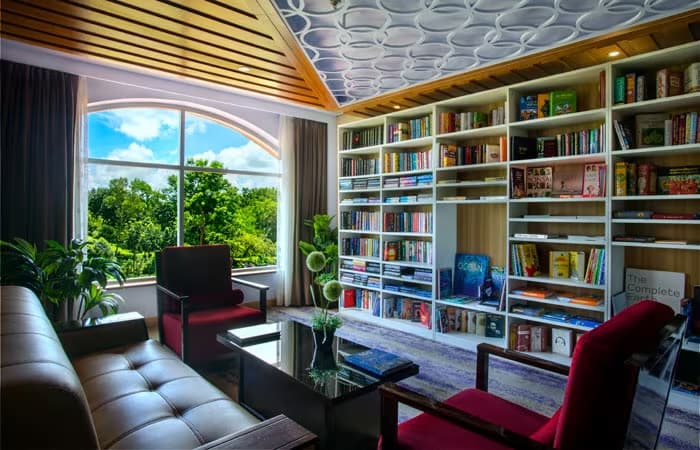 The resort's library lounge with red armchairs, a wall of shelved books, and an arched window over tea-garden trees