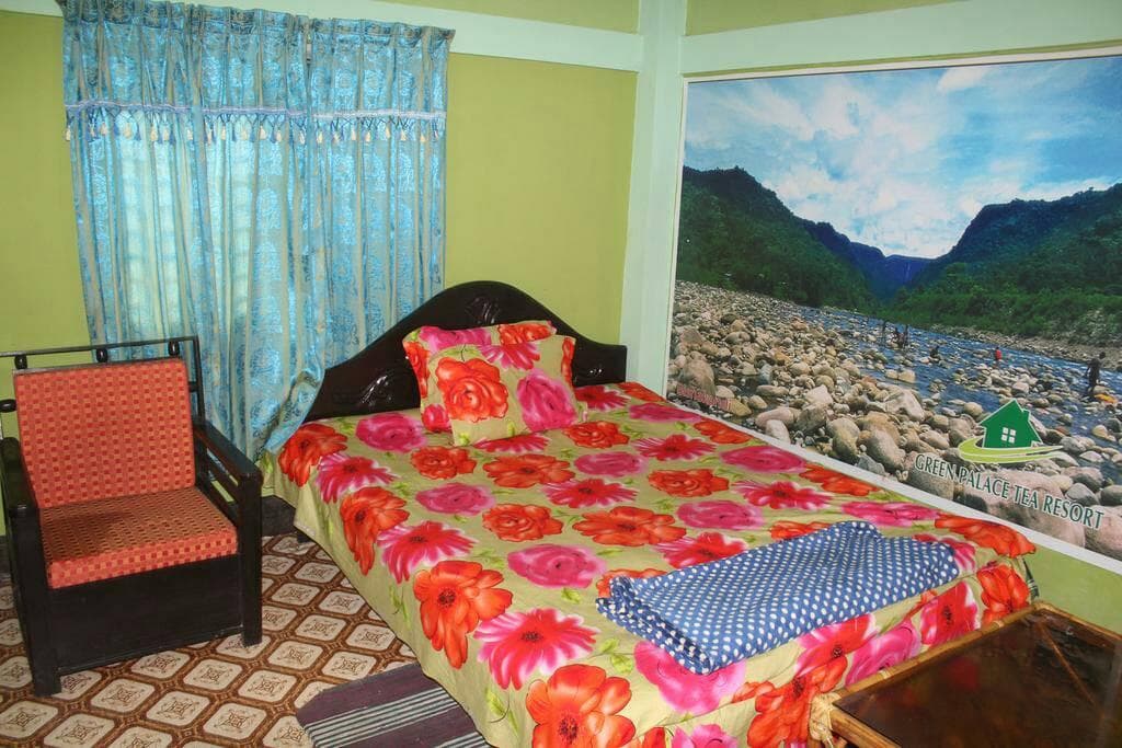 A guest room at Green Palace Tea Resort with a floral-print bed, blue curtains, and a wall mural branded with the resort's logo