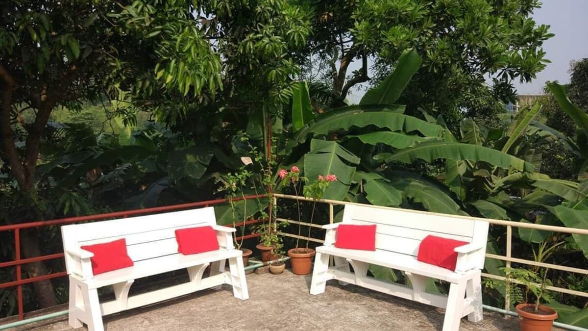 A rooftop seating area at Himachol Resort with two white benches and red cushions among banana plants
