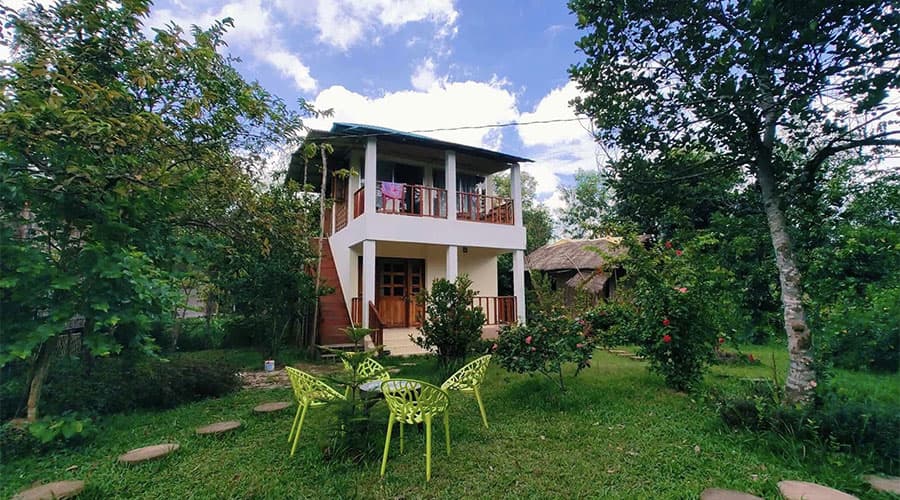 Himkuri Bon Bungalow's two-storey white cottage with a balcony, seen past a lime-green garden seating set