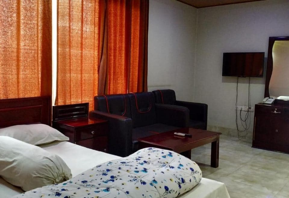 A twin-bed room at Hotel Mohsin Plaza with orange curtains, a black sofa, and a wall-mounted TV