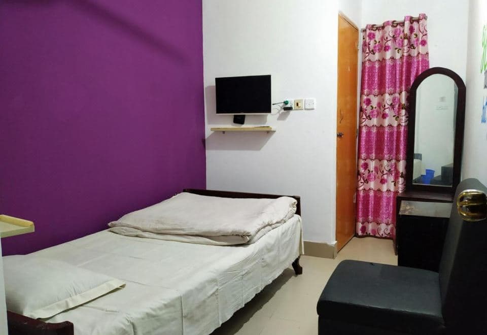 A single-bed room at Hotel Mohsin Plaza with a purple accent wall, wall-mounted TV, and a floral curtain by the door