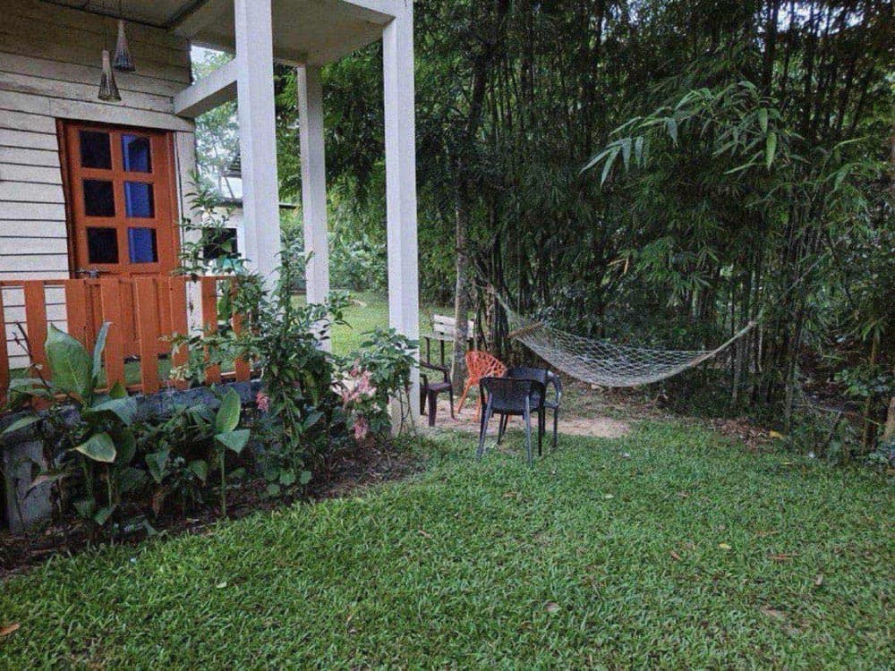 A garden porch with a hammock strung between bamboo at Jharna Tila