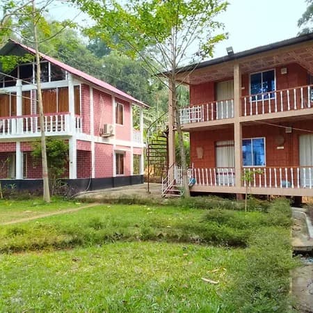 Two brick cottage buildings with wooden balconies at Madhabilata Eco Cottage, set in a garden lawn