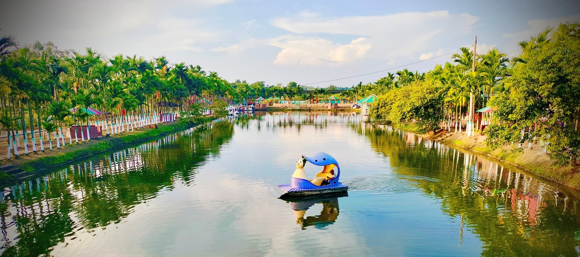 Palm-lined canal on the resort grounds with a duck-shaped paddle boat floating on the water