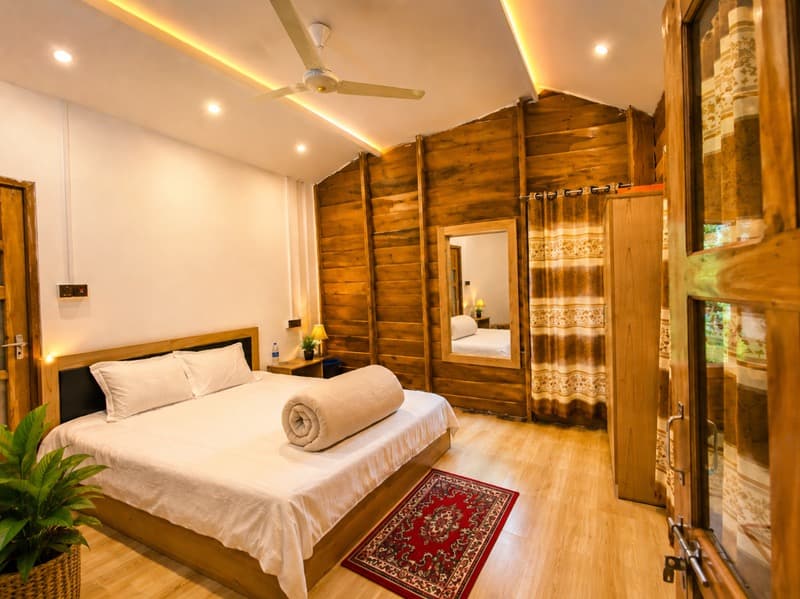 A wood-paneled bedroom at Nirban Nibash Resort with a white king bed, red patterned rug, and mirrored wardrobe