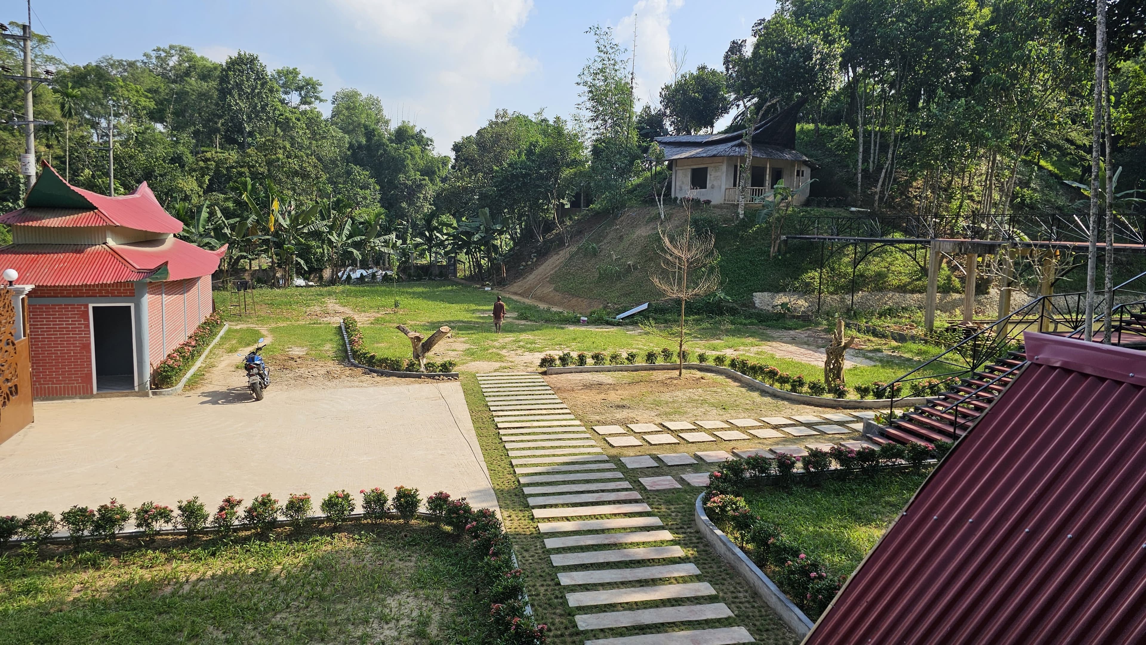 Grounds view of the red pagoda-roofed pavilion, garden pathway, and hillside cottages
