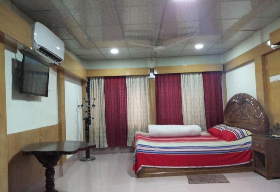 A guest room at Resort World with a red-and-white striped bed, wall-mounted TV, and maroon curtains