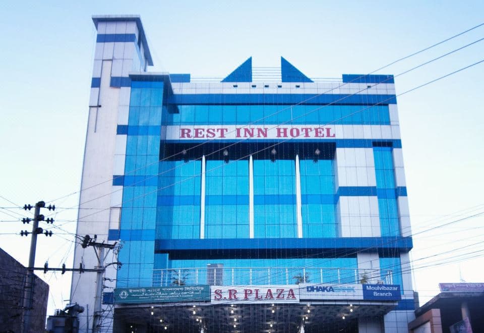 Rest Inn Hotel's blue-glass tower exterior with illuminated REST INN HOTEL signage above the S.R Plaza entrance
