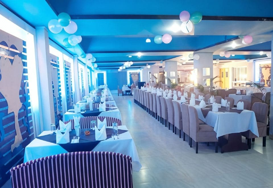 Long dining hall with rows of linen-covered tables and upholstered booth seating under a blue ceiling