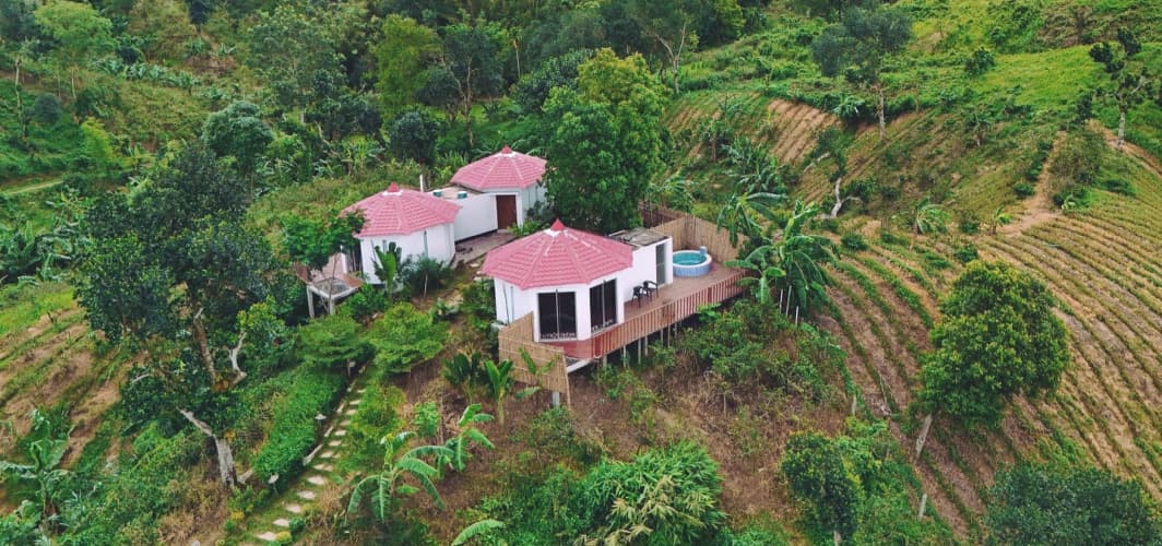 Aerial view of Rodela Eco Resort's three red-roofed conical cottages on a tea-garden hillside, with a small round plunge pool on the connecting deck