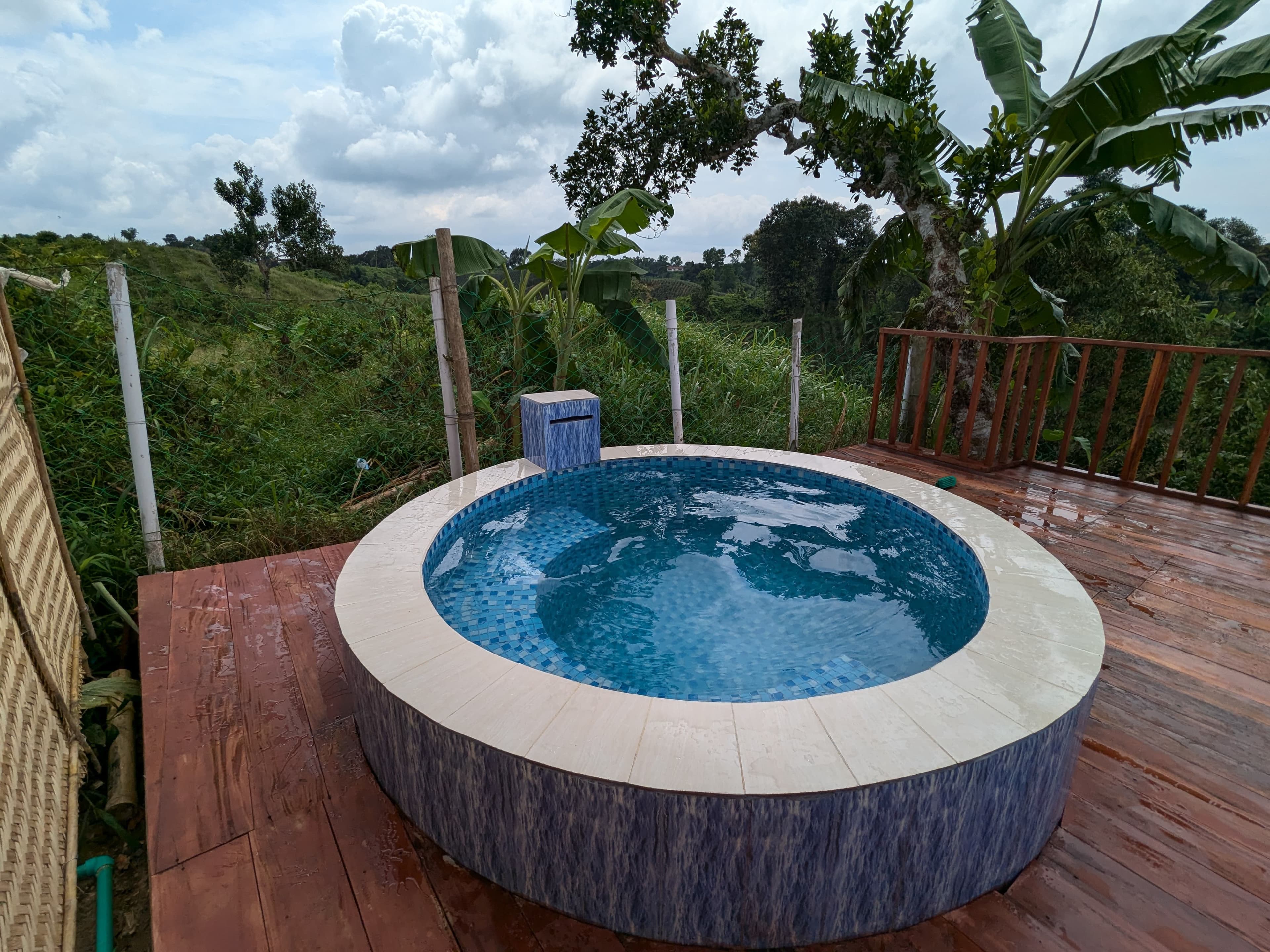 Close-up of the round blue-and-white mosaic-tiled plunge pool on the wooden deck, overlooking the fenced garden and hillside