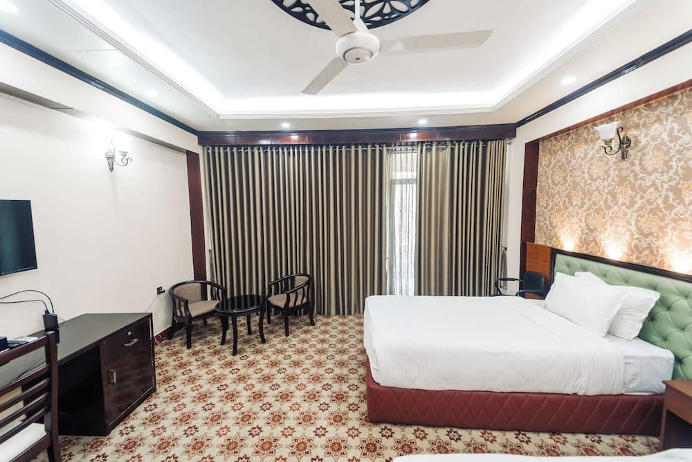 Guest room with a green tufted headboard, wood-paneled accent wall, striped curtains, and matching patterned carpet
