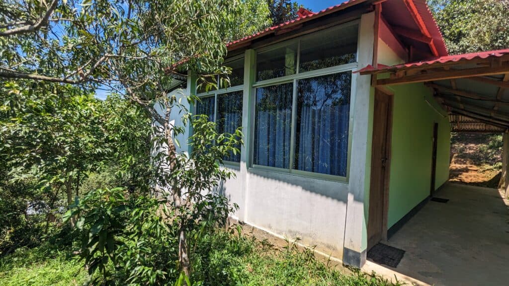 A red-roofed cottage at Shanti Bari with large curtained windows, tucked among trees