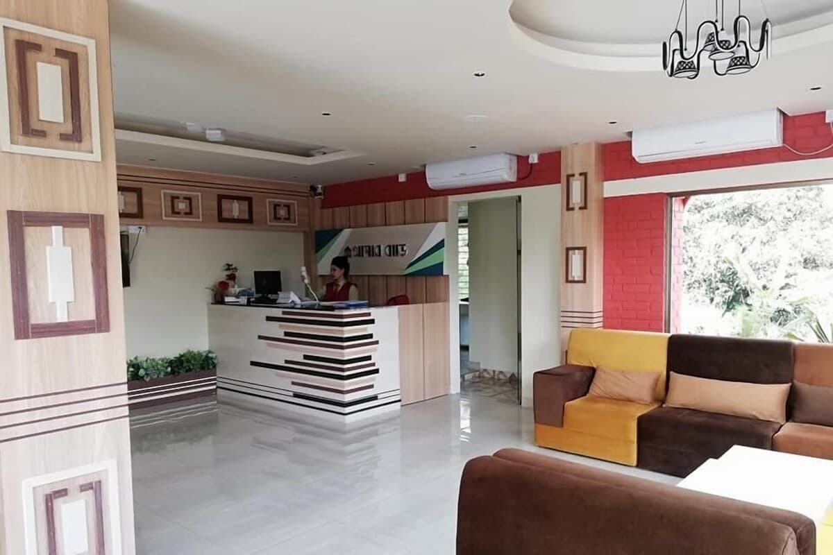 Hotel reception lobby with a wood-panelled front desk, staff member at the counter, red accent wall, and a mustard-and-brown sofa seating area