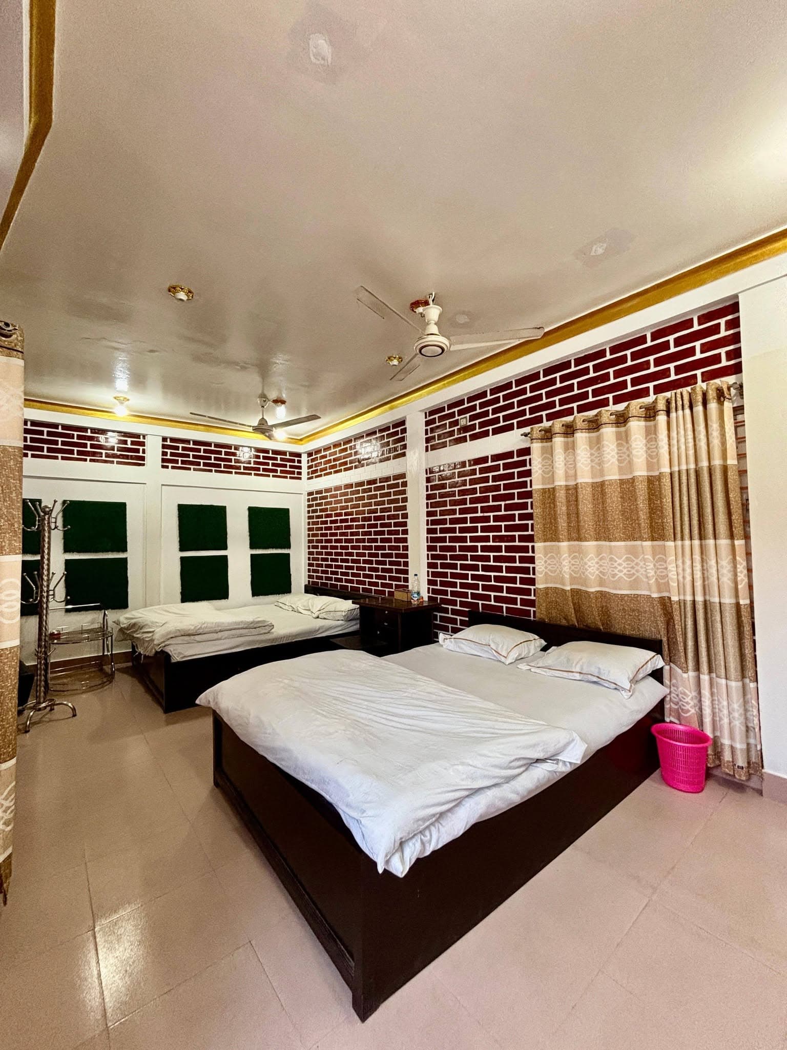 Family room with two double beds, dark red brick-pattern accent wall, ceiling fans, and a coat rack