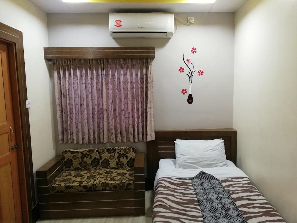 A single-bed guest room at Sultan Restaurant & Guest House with a built-in wooden bench sofa, floral curtains over the window, a wall-mounted Singer air conditioner and a red flower decal on the wall