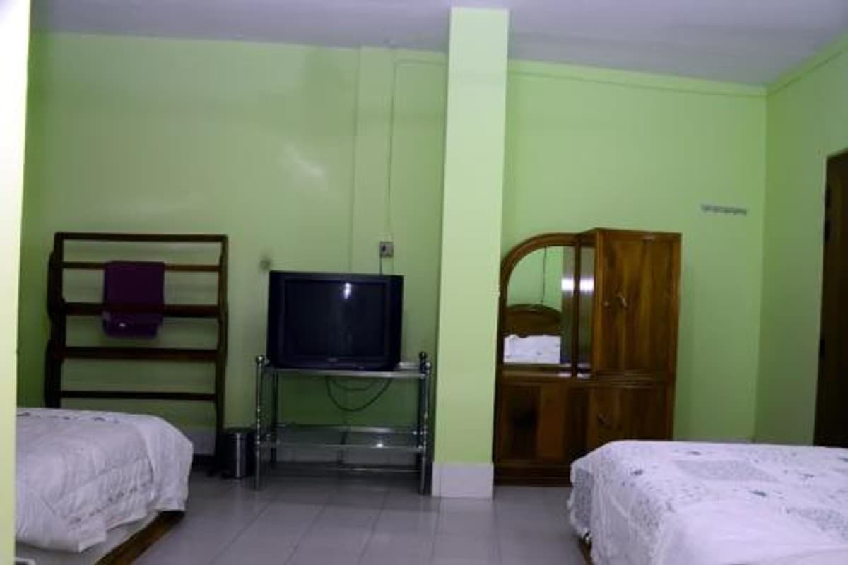Twin-bed guest room in mint green with an older CRT television on a glass trolley and a tall wardrobe with an oval mirror