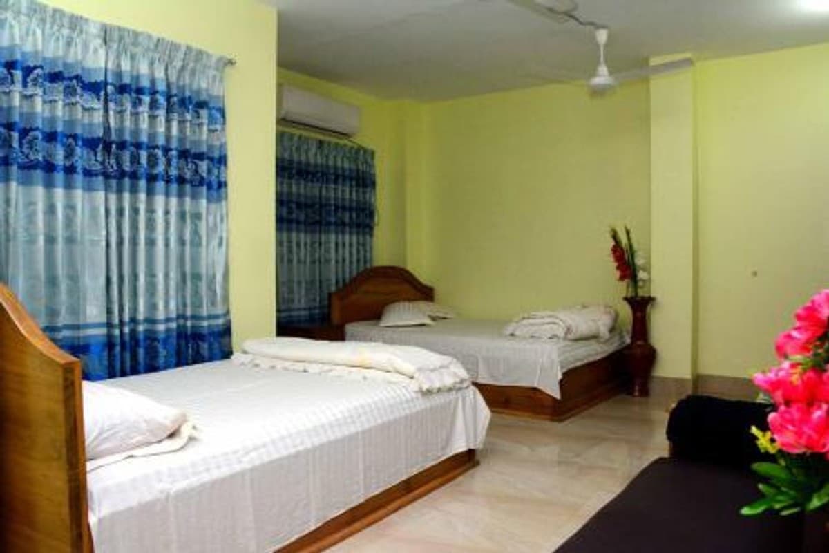 Pale yellow twin room with a ceiling fan, blue patterned curtains, and artificial flowers on the bedside table
