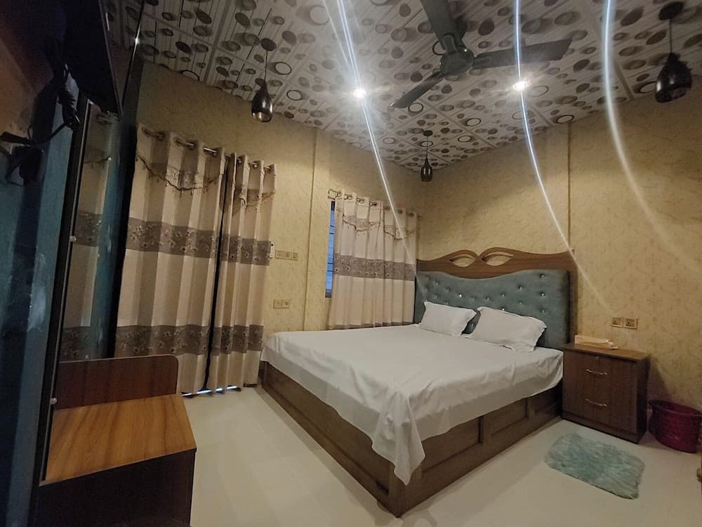 Guest room with a grey tufted headboard, patterned ceiling tiles, and curtained window