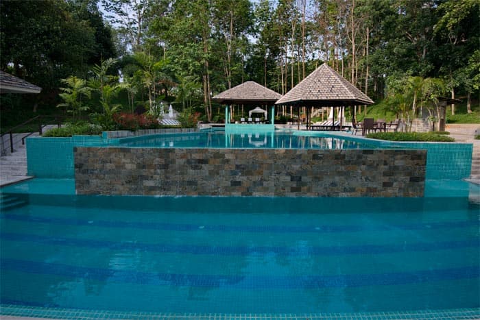 DuSai Resort & Spa's infinity-edge pool with a thatched-roof pavilion and sun loungers, backed by forest