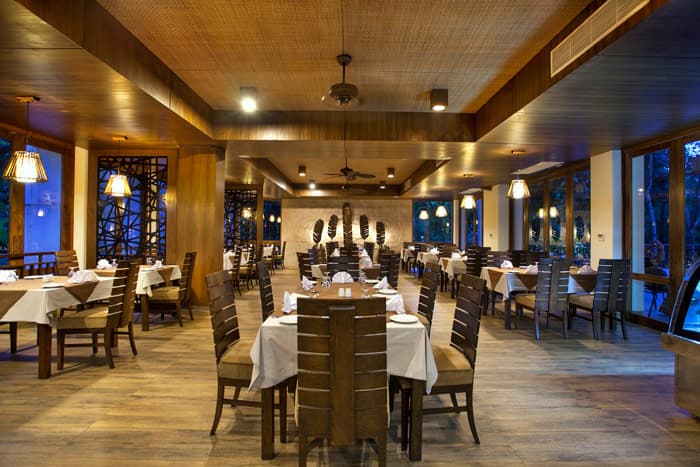 DuSai Resort & Spa's wood-panelled restaurant set with white tablecloths, seen at dusk through floor-to-ceiling windows