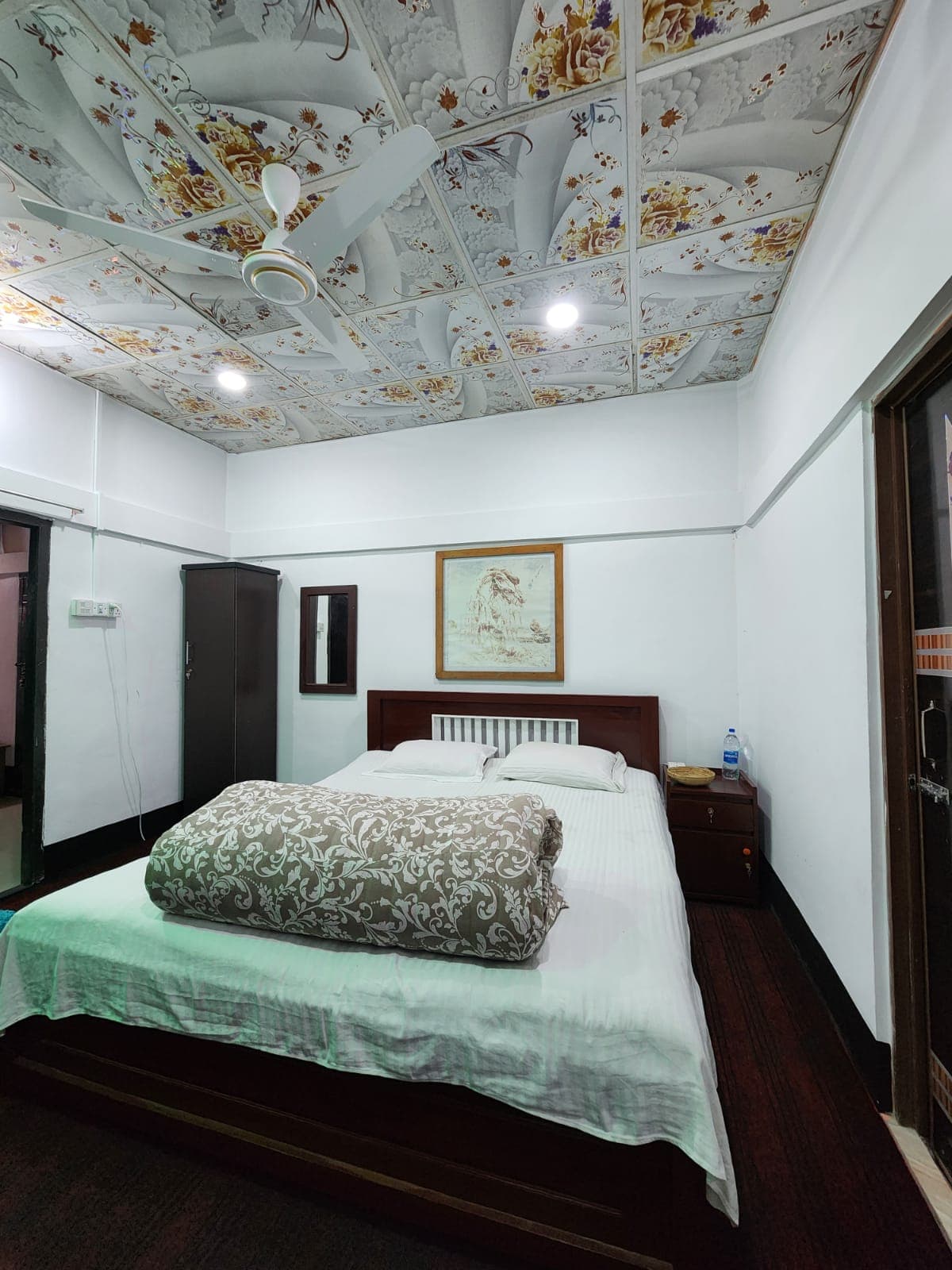 Guest room with an ornate floral-patterned ceiling, a wardrobe, wall mirror, and a landscape painting above the headboard